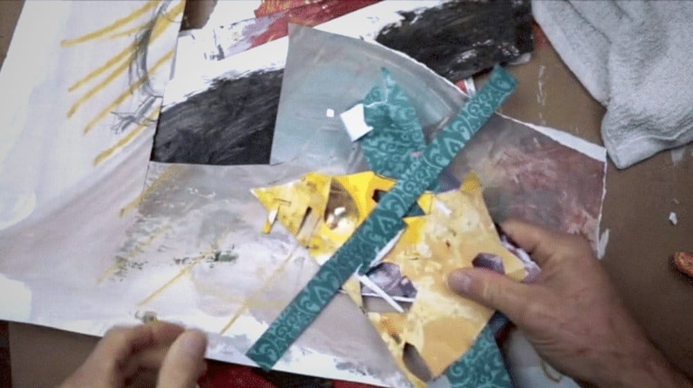 Robert Joyner holding sheets of handmade collage paper in his art studio, ready for a mixed media project.